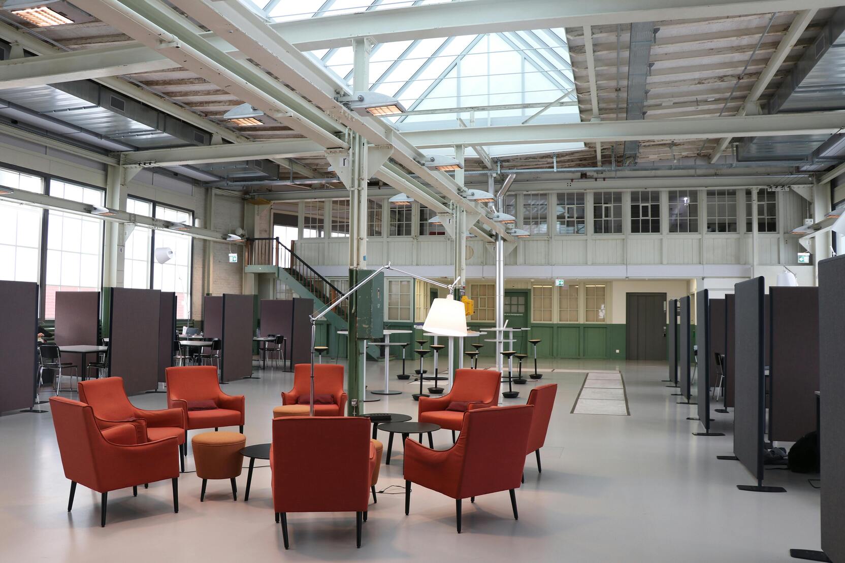 Modern gestalteter Raum mit roten Sesseln und Tischen, umgeben von Trennwänden und großen Fenstern für Tageslicht.