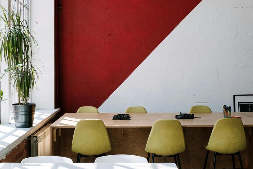 Moderne B&uuml;roumgebung mit einem langen Tisch, gelben St&uuml;hlen und einer roten Wand mit diagonalem Farbblock.